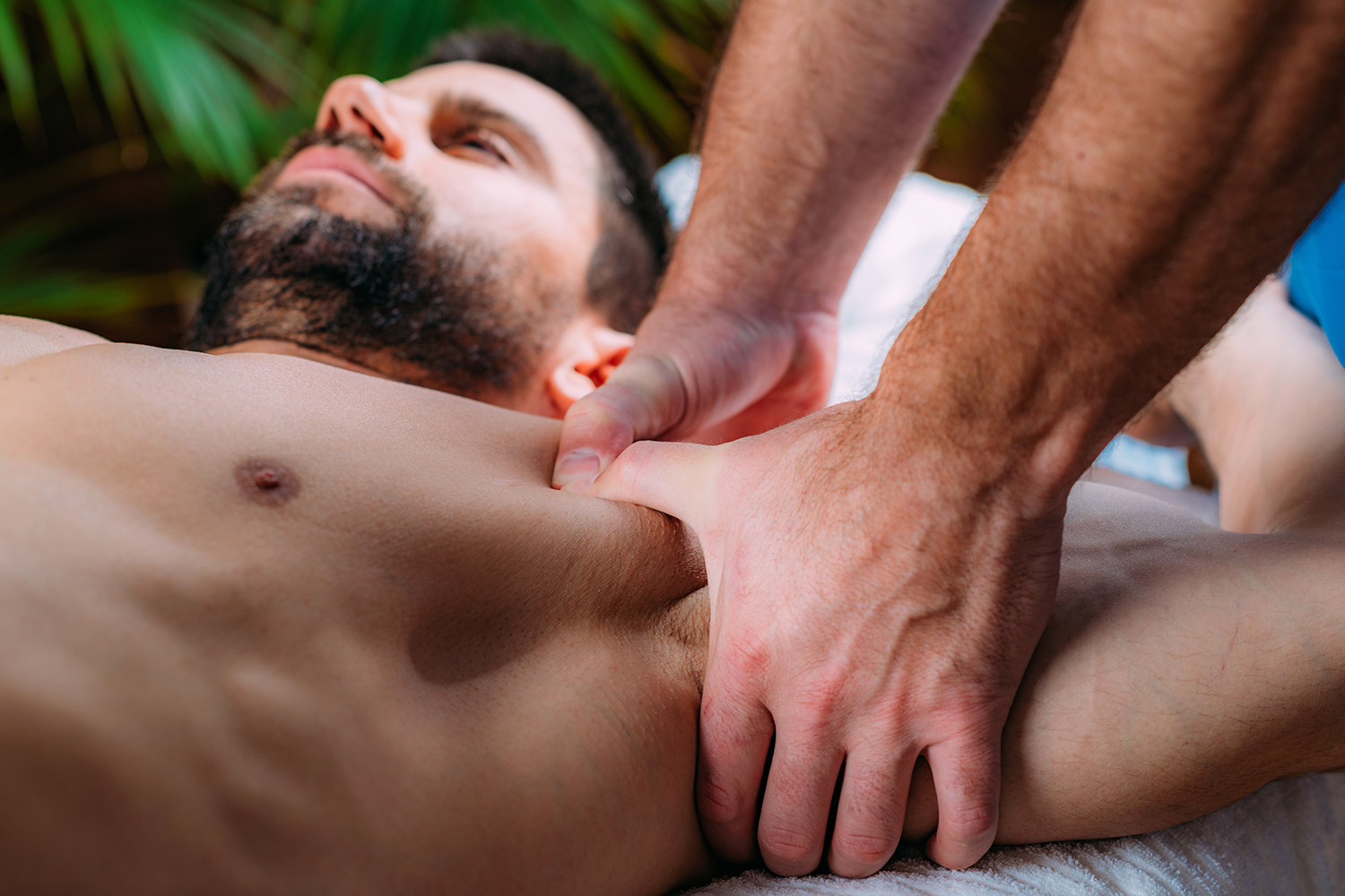 Man receiving deep tissue massage, therapist applying pressure on shoulder area, emphasizing muscle relaxation and pain relief.